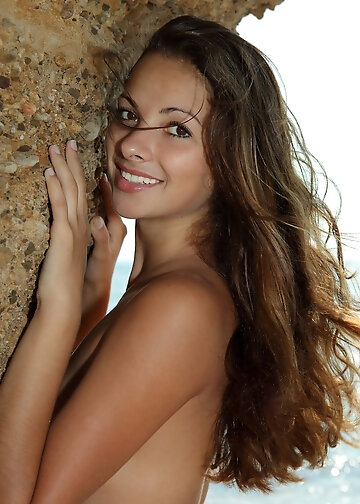 Wild angel with flowing brown hair looks her best posing on the rocky beach